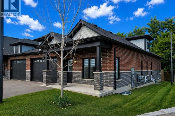 Exterior view of townhouse showing brick and stone details, with a circular driveway and nearby homes. - 16 Brookfield Lane, Simcoe