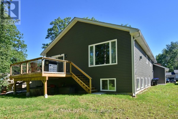 Rear exterior of the house showing dark grey siding, a wooden deck with railings, and backyard. - 16 Caribbean Drive, Wasaga Beach
