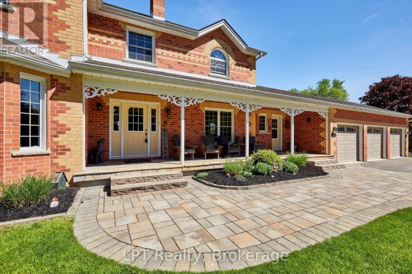 Brick house exterior with a covered porch, yellow door, and paved driveway with garage. - 16 Cawkers Cove Road, Scugog