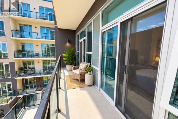 Balcony with wicker chair and side table overlooking apartment complex courtyard and buildings. - 16 Concord Place Unit# 427, Grimsby
