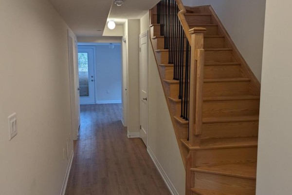 Interior hallway with light wood laminate flooring and oak staircase with black spindles. - 16 Coote Court, Ajax