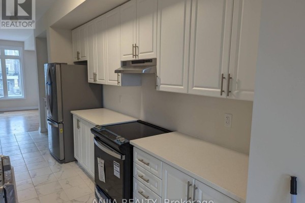 Modern white kitchen with stainless steel refrigerator, black stove, and white quartz countertops. - 16 Coote Court, Ajax