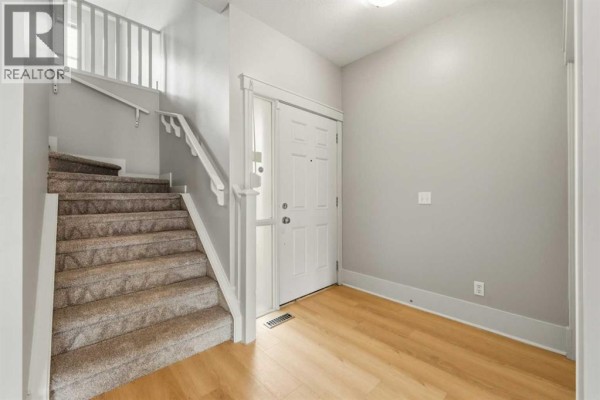 Interior entryway with light wood flooring, a white front door, and carpeted stairs. - 16 Cougartown Place Sw, Calgary