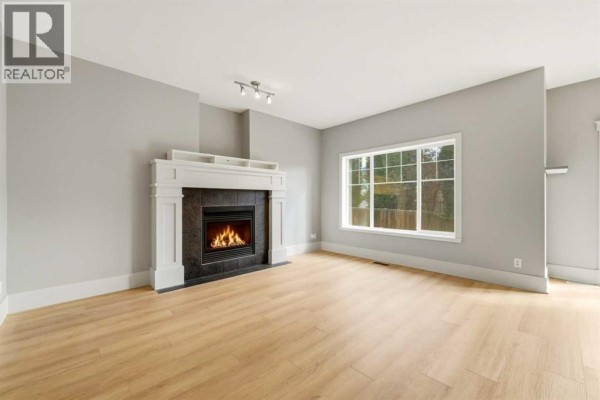 Living room featuring a gas fireplace with a white mantel and large window. - 16 Cougartown Place Sw, Calgary