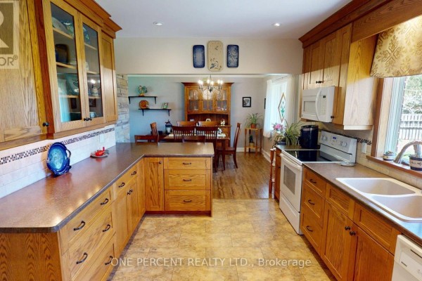 A wide view of the kitchen showing oak cabinets, a white refrigerator, and a doorway leading to a staircase. - 16 Daleview Crescent, Pelham