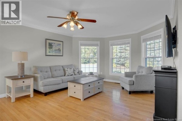 Living room with light grey walls, wood floors, grey sofa, armchair, and bay windows. - 16 Darling Court, Quispamsis