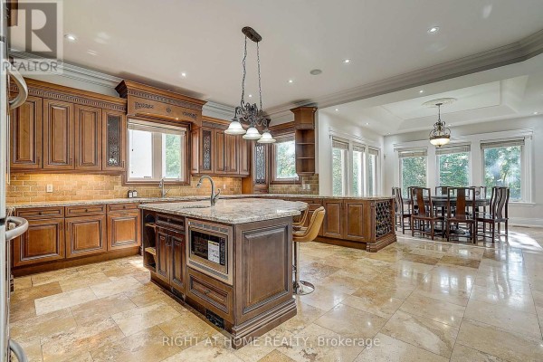 Kitchen island with microwave, granite counters, and ornate cabinetry, adjacent to dining area with chandelier. - 16 Fairview Avenue Richmond Hill