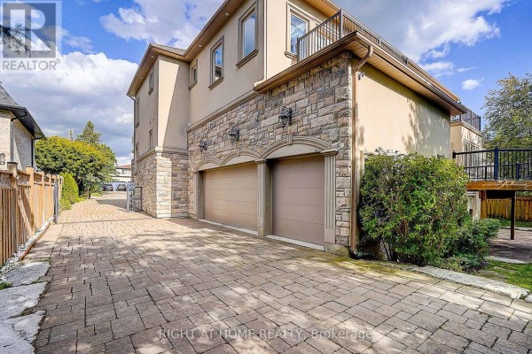 Side view of a house showing a three-car garage with tan doors, stone facade, and paved driveway. - 16 Fairview Avenue, Richmond Hill