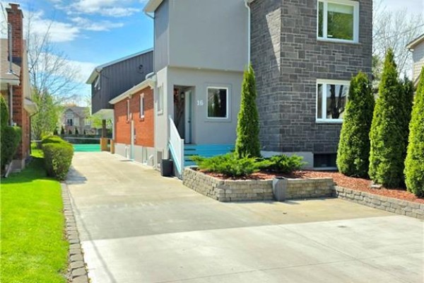 Front exterior of a house with grey stone and brick, a paved driveway, and manicured landscaping. - 16 Forest Hill Road, St  Catharines