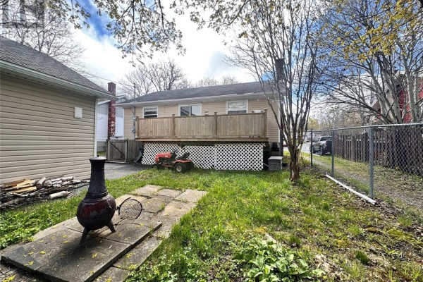 Backyard of a beige bungalow with a wooden deck, fire pit, and grass. - 16 Hatcher Street, St  John S