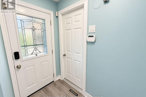Interior entrance hallway with light blue walls, a white front door with decorative glass, and a white interior door. - 16 Joshua Court, Brampton