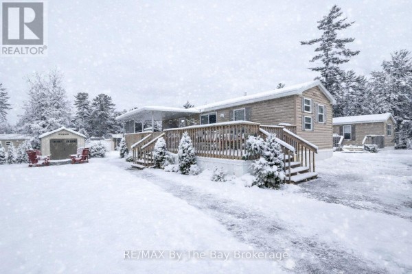 Mobile home covered in snow, with wooden deck and snow-covered yard. - 16 Kenora Trail, Wasaga Beach