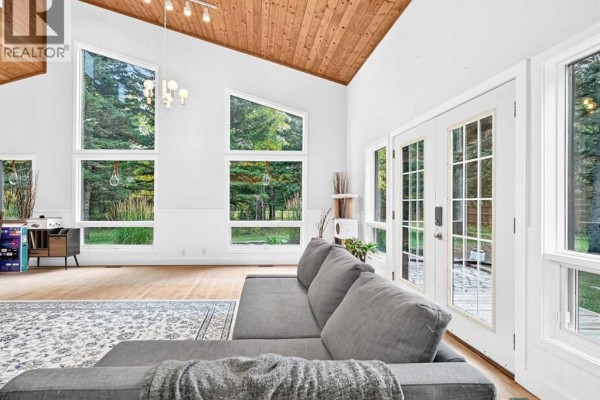 Living room with a grey sectional couch, large windows, and wood ceiling. - 16 Mountain View Park, Bragg Creek