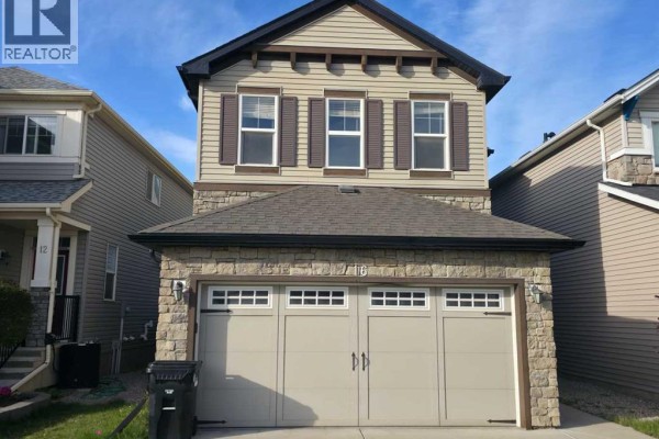 Exterior view of a two-story house with beige siding, stone accents, and a tan double garage door. - 16 Nolancrest Green Nw, Calgary