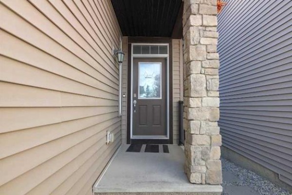 Close-up of the front entrance door with a glass pane and stone column. - 16 Nolancrest Green Nw, Calgary