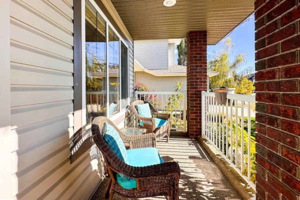 Covered front porch with two wicker chairs with blue cushions and a small glass table. - 16 Normandeau Cr, St  Albert