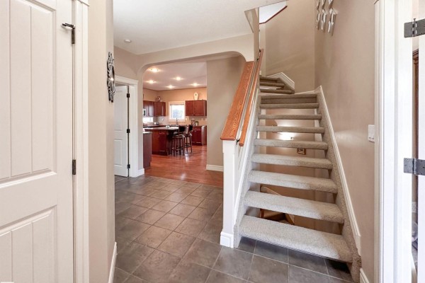 Entryway with tile flooring and a carpeted staircase leading upstairs, with a view into the kitchen. - 16 Normandeau Cr, St  Albert