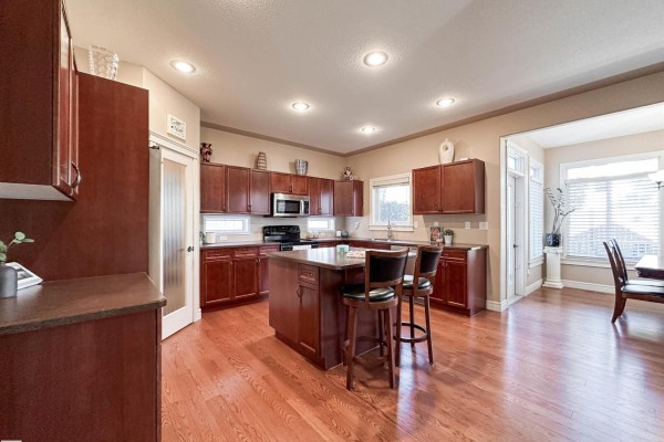 Spacious kitchen with dark wood cabinets, stainless steel appliances, and a large central island with stools. - 16 Normandeau Cr, St  Albert