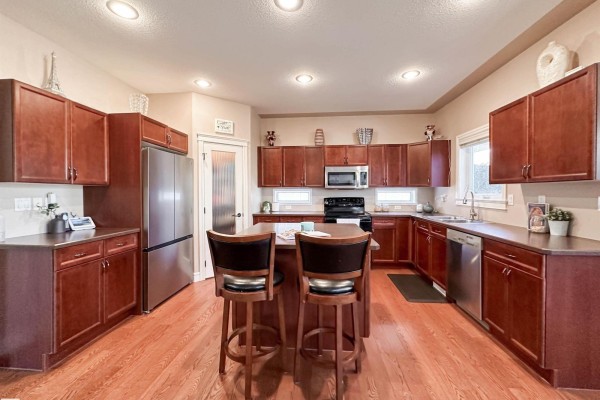 Kitchen with dark wood cabinetry, stainless steel appliances including a refrigerator, and an island with seating. - 16 Normandeau Cr, St  Albert