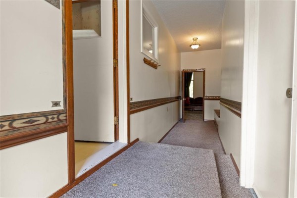 Interior hallway with beige walls, patterned wallpaper, and grey carpet. - 16 Pine Crescent, Steinbach