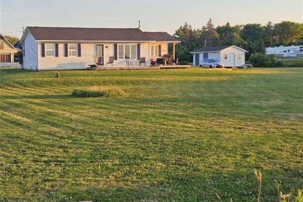 Wide shot of the white bungalow and surrounding green lawn under a blue sky. - 16 Spence's Beach Road, Murray Corner
