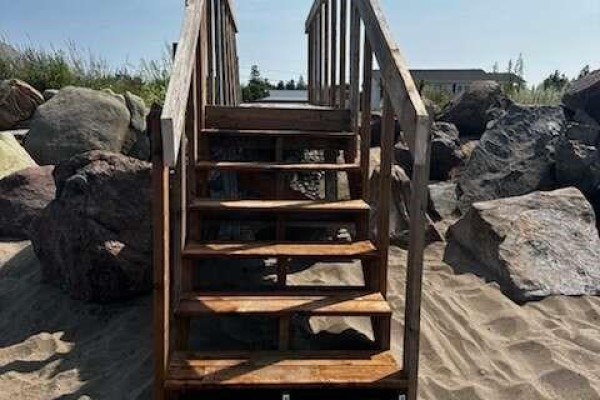 Wooden stairs lead down to a sandy beach, flanked by large grey rocks. - 16 Spence's Beach Road, Murray Corner
