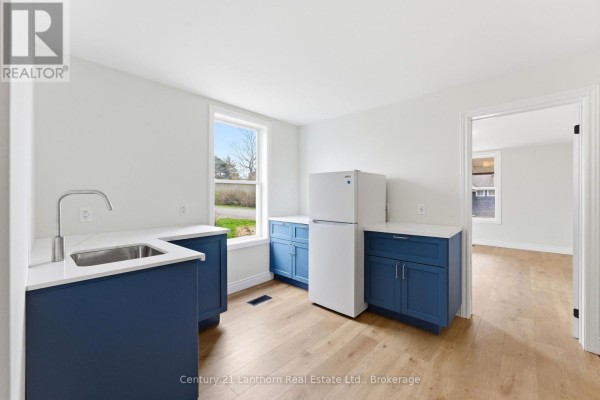 Kitchenette area with blue cabinets, white countertop, sink, and a white refrigerator, opening to another room. - 16 Store Street, Prince Edward County