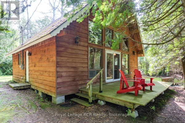 Front view of the cabin with a wooden deck and two red Adirondack chairs. - 16 Youngs Drive, South Bruce Peninsula