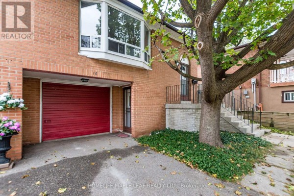 Close-up of red garage door on a brick house with a large tree in front. - 16 Zealand Road, Toronto