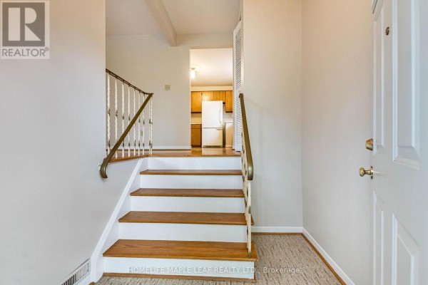 Interior foyer with wood stairs, white walls, and a view into the kitchen. - 16 Zealand Road, Toronto