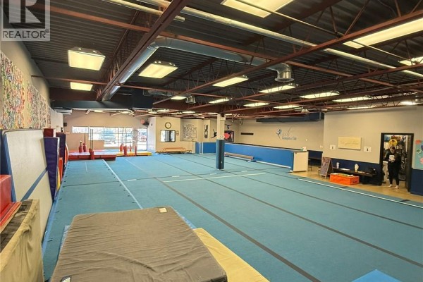 Wide view of gymnastics facility showing blue mats, padding, and equipment with wall decals. - 160 Brantwood Park Road Unit# 1a, Brantford