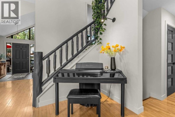 Interior entryway with a black digital piano and stool beside a wooden staircase with black spindles. - 160 Carey, Canmore