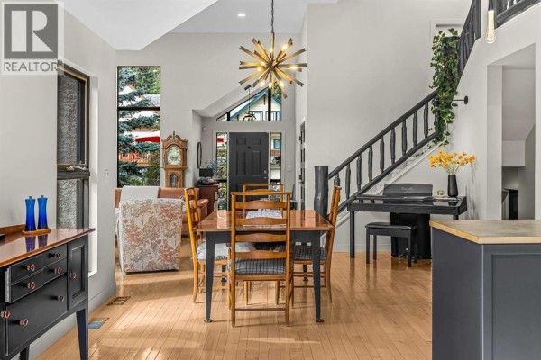 Open-concept living and dining area with light wood floors, a wooden dining table, and a staircase. - 160 Carey, Canmore