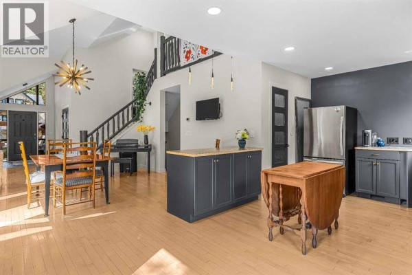 Spacious kitchen and dining area with light wood floors, dark cabinetry, a stainless steel refrigerator, and a drop-leaf table. - 160 Carey, Canmore