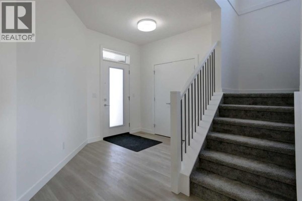 Interior entryway with a glass front door, light wood-look flooring, and carpeted stairs. - 160 Copperhead Road Se, Calgary
