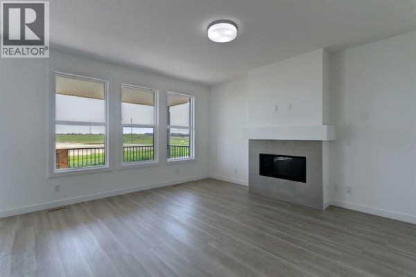 Living room with a modern gas fireplace, large windows, and light wood-look flooring. - 160 Copperhead Road Se, Calgary