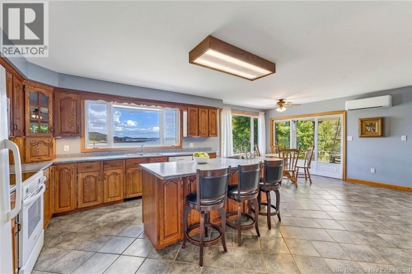 Kitchen with oak cabinets, granite countertops, island with seating, and tiled floor. - 160 Harkness Road, Chamcook