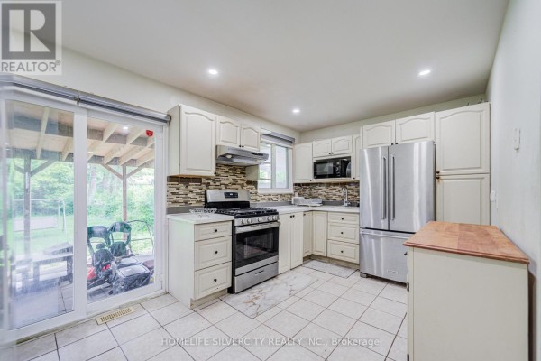 Kitchen with white cabinets, stainless steel appliances, and a sliding glass door opening to a deck. - 160 Purvis Crescent, Toronto
