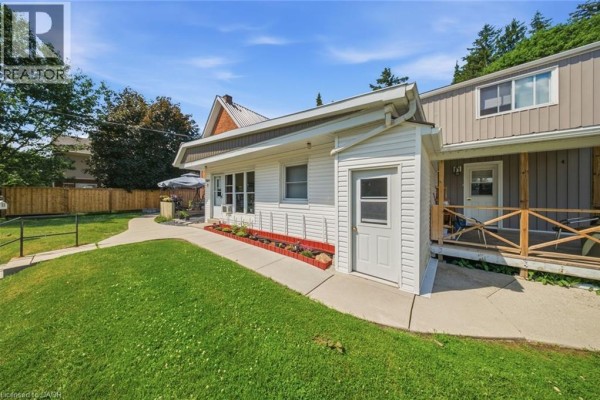Side view of the multi-family house showing white siding and a small storage door. - 160 Queen Street, Simcoe