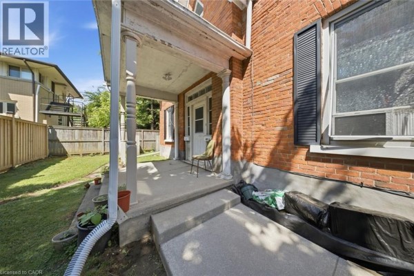 Covered front porch of the brick section of the house with a concrete floor and white columns. - 160 Queen Street, Simcoe