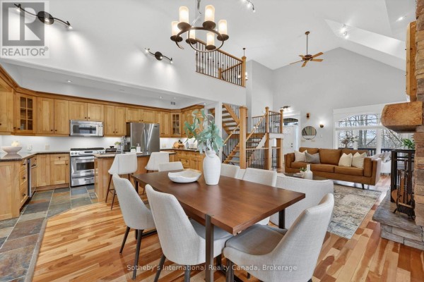 Open-concept living area with kitchen, dining table, sofa, stone fireplace, and vaulted ceilings - 160 Sunset Boulevard Blue Mountains