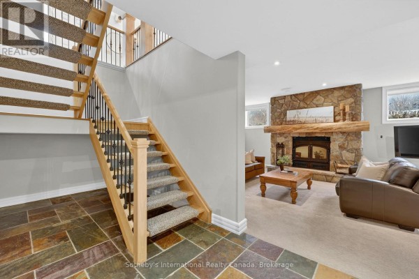Split staircase with stone tile and carpet, leading to living room with stone fireplace and leather sofas.