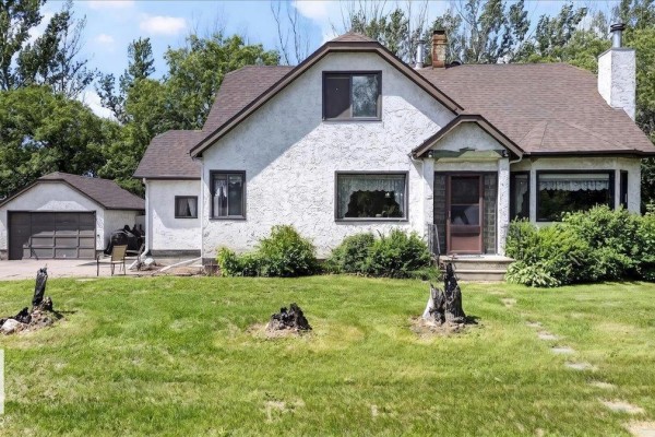 Front view of a white stucco house with a brown roof, attached garage, and green lawn. - 160005 Twp 540, Rural Lamont County