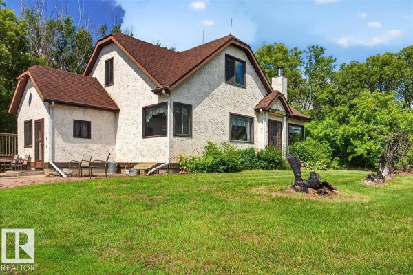 Side view of a white stucco house with a brown roof, green lawn, and surrounding trees. - 160005 Twp 540, Rural Lamont County