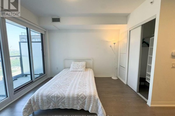 Bedroom area with a single bed, sliding closet doors, and a large window with city views. - 1601 - 251 Jarvis Street, Toronto