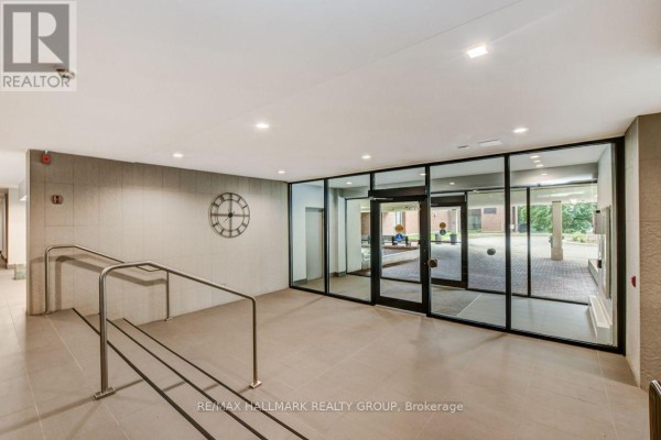 Building lobby with beige tiled floors, beige walls, glass doors, and a decorative clock. - 1601 - 665 Bathgate Drive, Ottawa