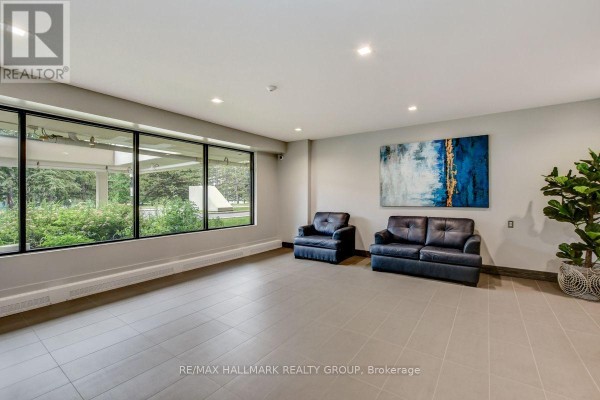 Building lobby seating area with two dark leather chairs, a sofa, large windows, and abstract art. - 1601 - 665 Bathgate Drive, Ottawa