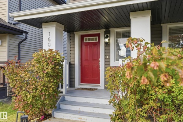 View of a red front door with sidelights and a covered porch with pillars. - 16012 11 Av Sw Sw, Edmonton