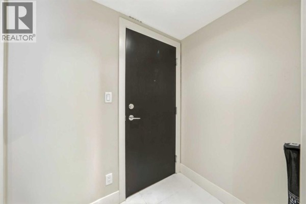 Interior view of a narrow hallway with a dark brown apartment door and light grey walls. - 1602, 1111 10 Street Sw, Calgary