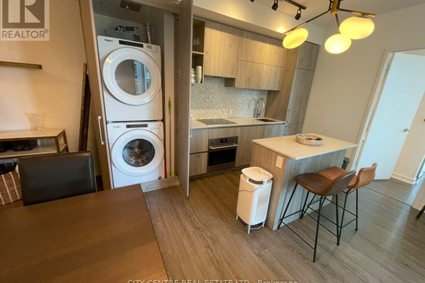 Kitchen with stacked washer and dryer unit next to cabinetry and dining area. - 1602 - 1 Yorkville Avenue, Toronto